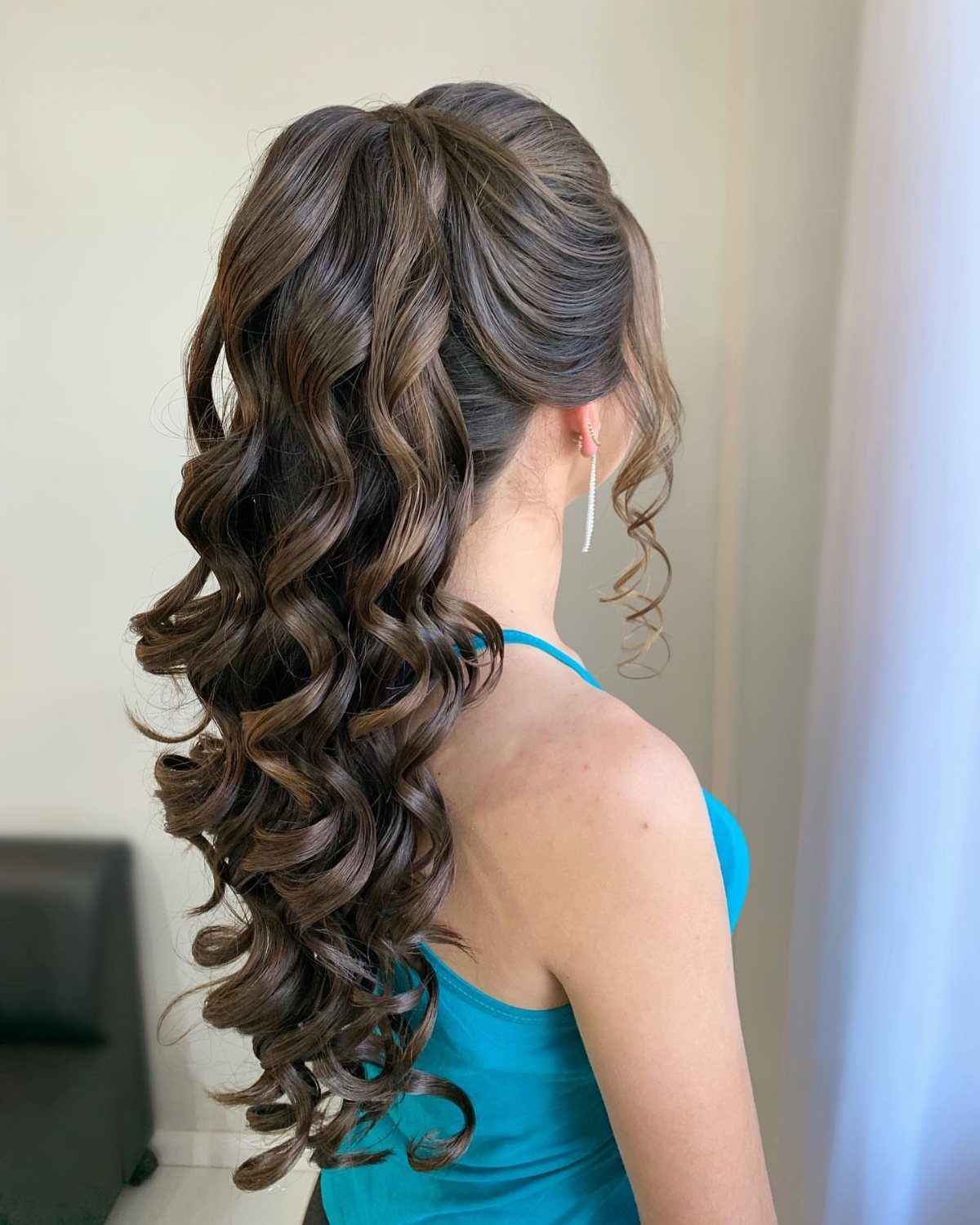 Woman with long brown hair in a high curly ponytail cascading down her back.