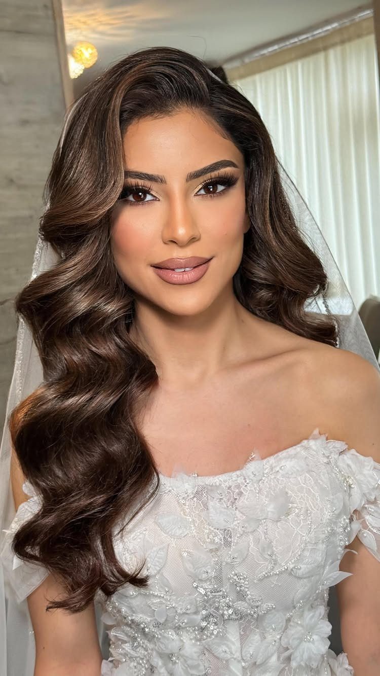 Woman with long brunette loose waves wearing a white floral wedding dress and veil.