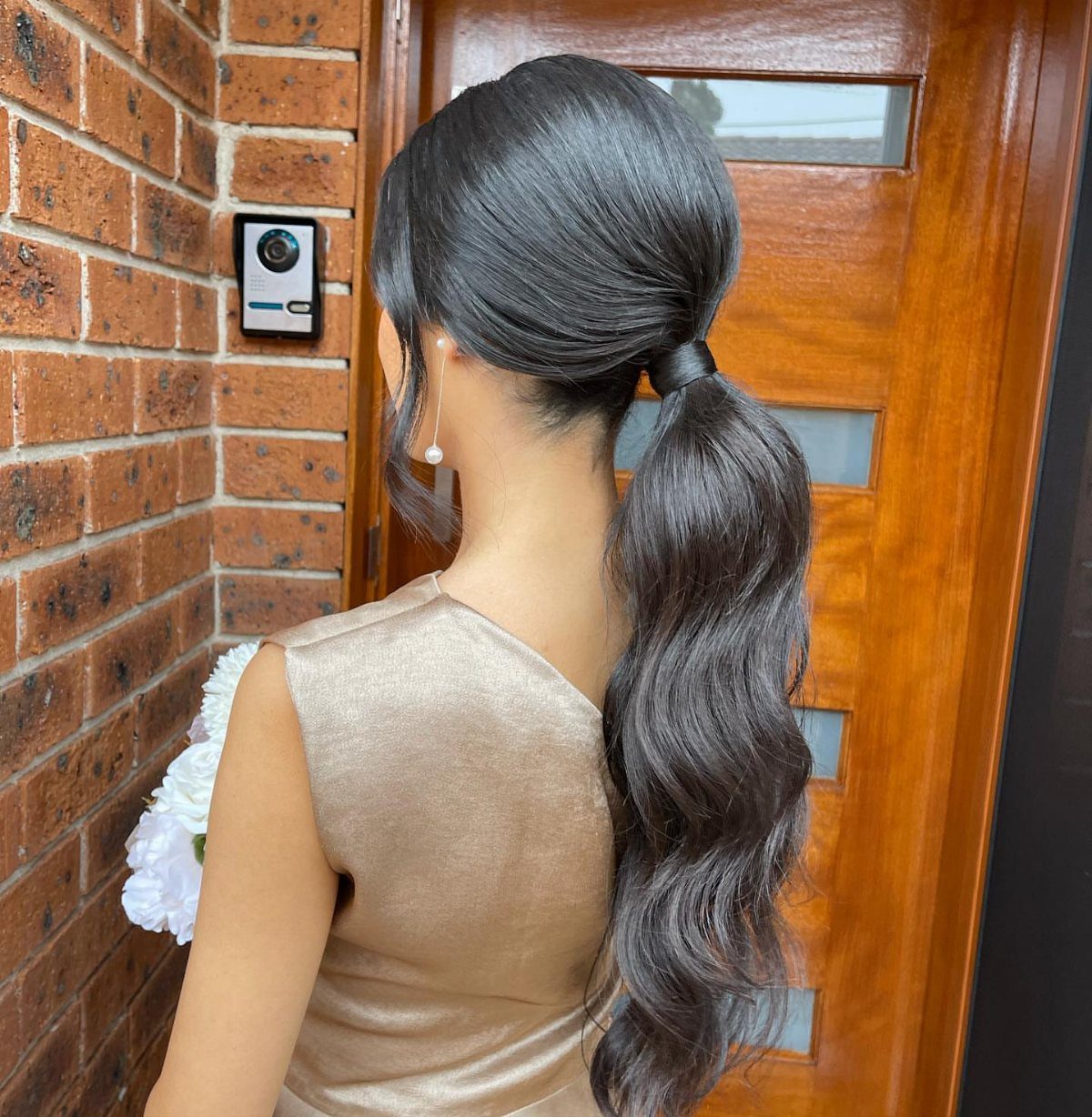 Woman with dark wavy hair styled in a low ponytail wearing a gold dress.