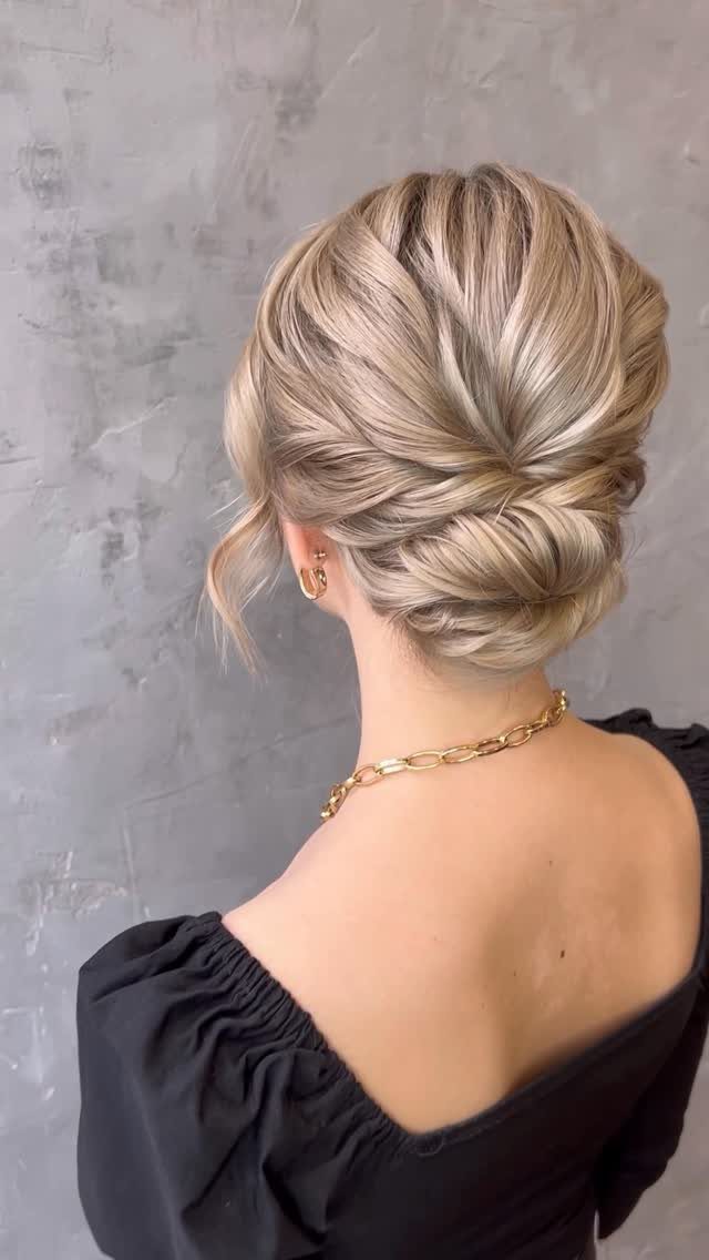 Blonde hair styled in a low twisted updo with a gold chain necklace.