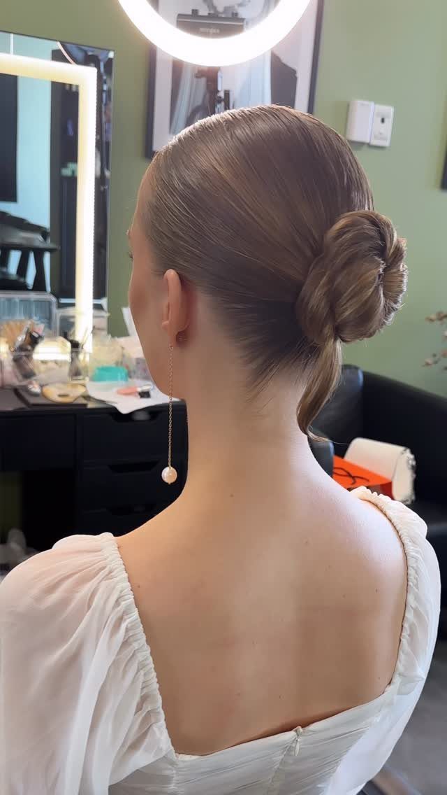 Woman with blonde hair styled in a sleek low bun and white dress.