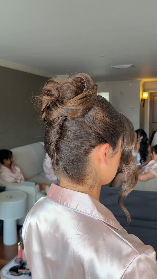 Woman with brown hair in a high textured bun and side braid.