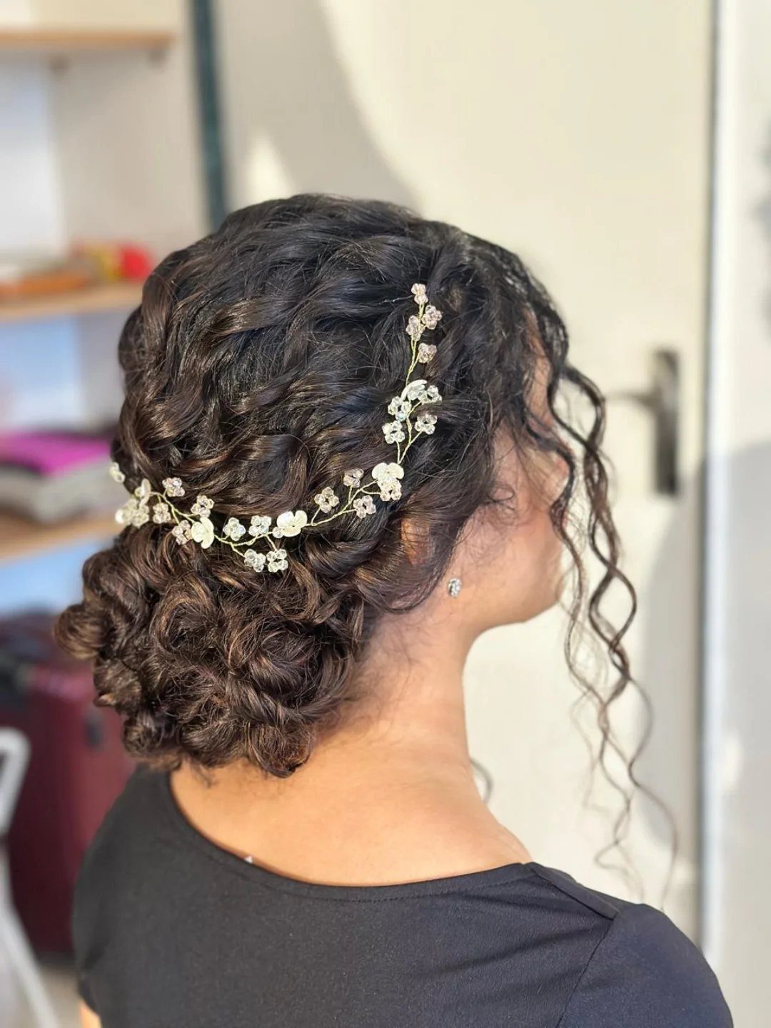 Dark curly hair styled in a low bridal bun with a white floral vine.