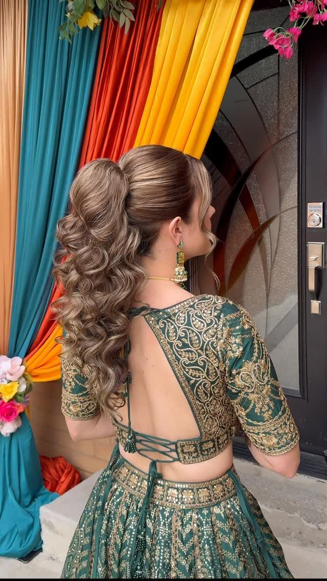 Woman with a high voluminous curly ponytail wearing a green embroidered Indian dress.