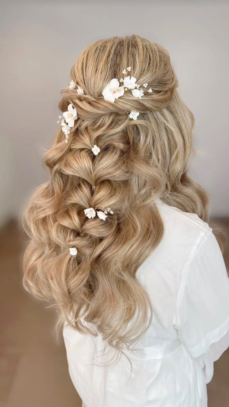 Blonde curly hair in a half-up style decorated with small white floral hairpins.