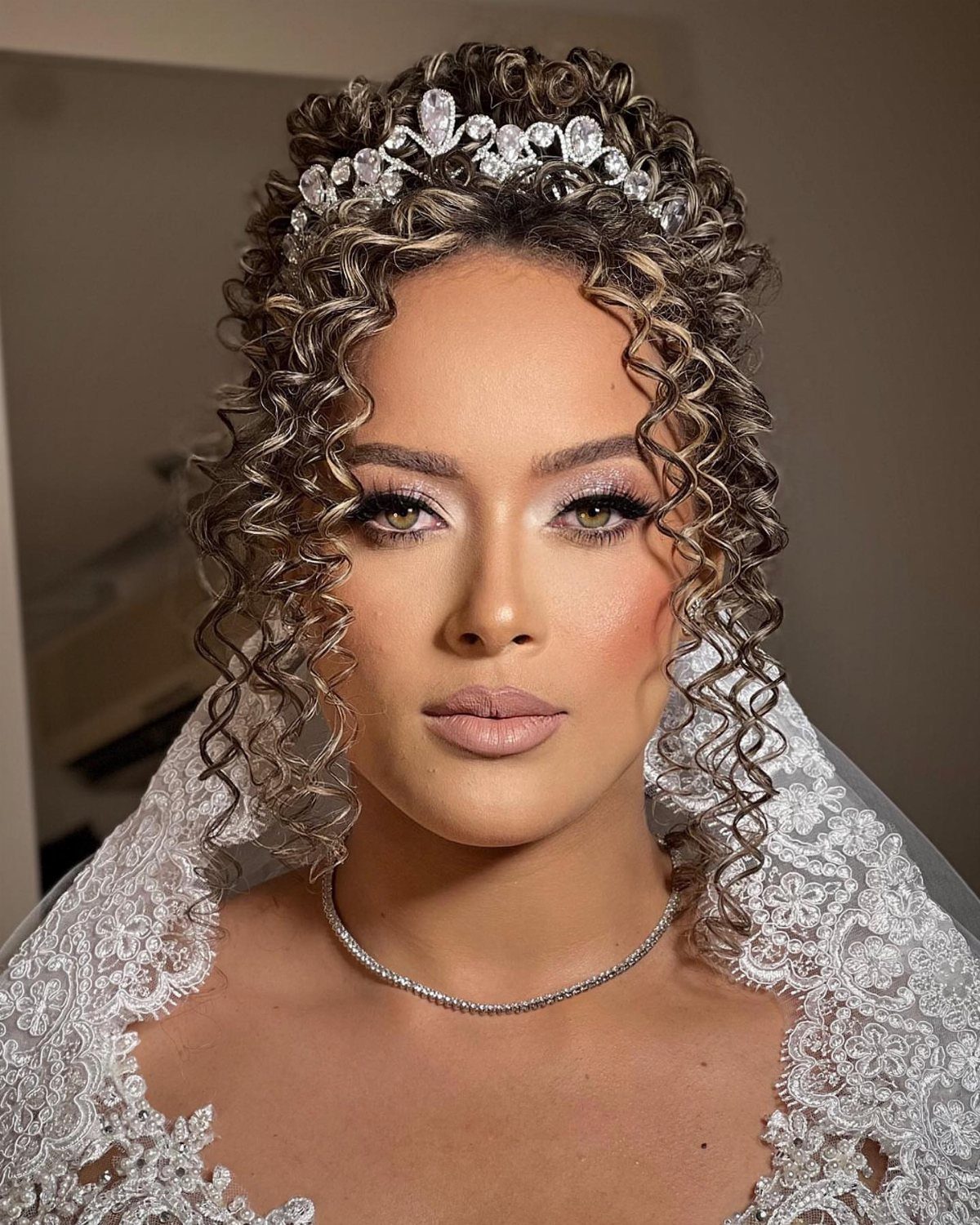 Woman with curly brown hair wearing a sparkling crystal headband and white lace gown.