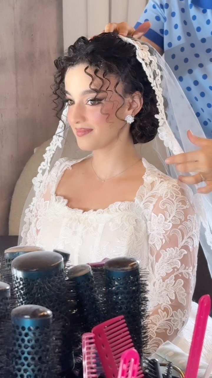 Bride with dark curly updo wearing a white lace wedding veil and dress.