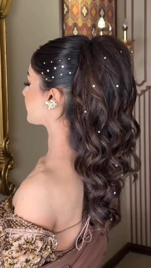 Woman with a high voluminous curly ponytail decorated with small white pearls.
