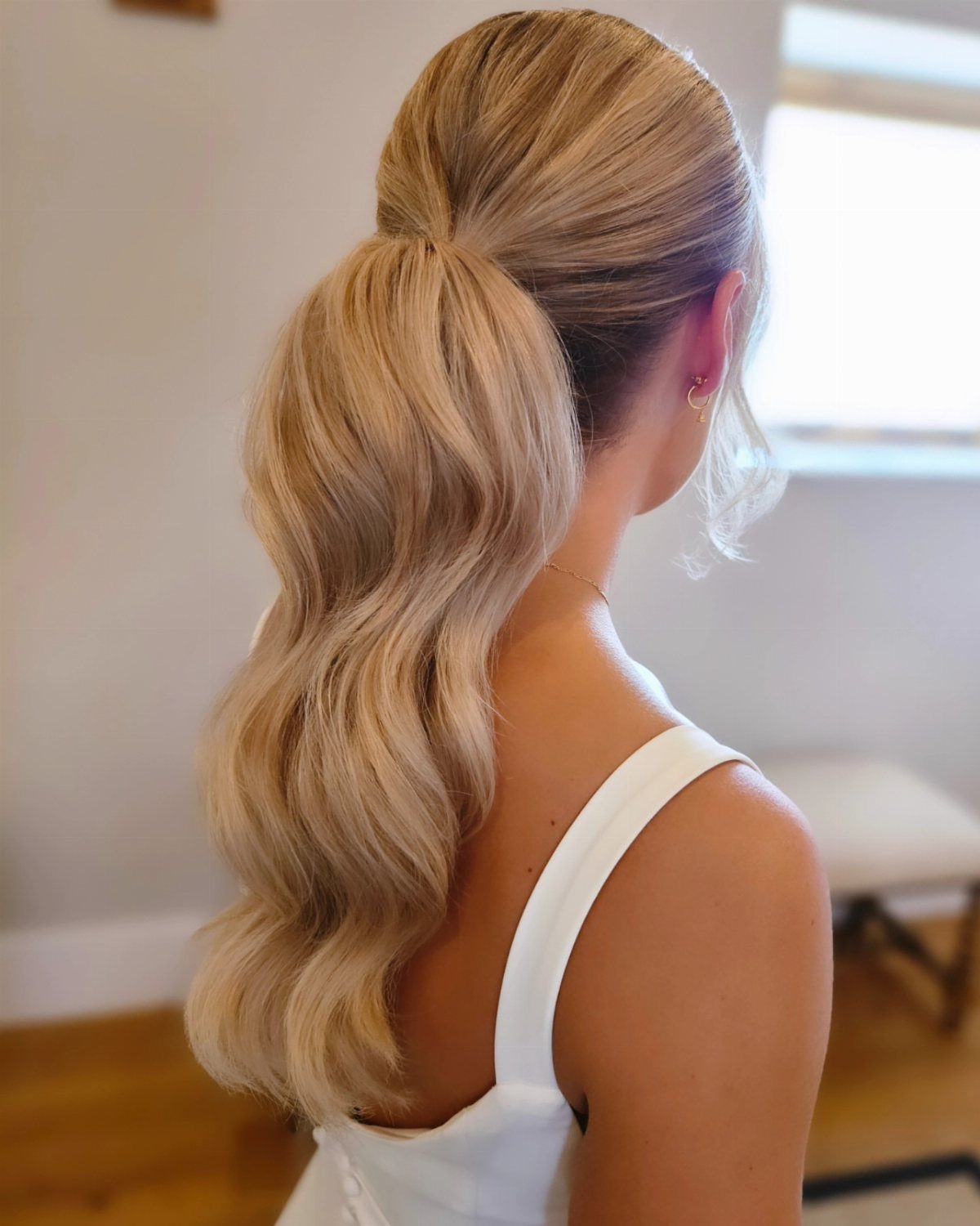 Blonde woman with curly low ponytail hairstyle wearing a white sleeveless dress.