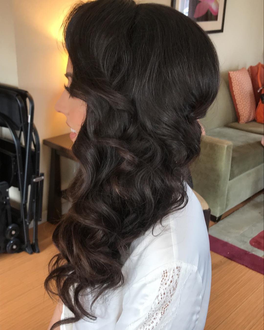 Woman with long dark brown hair styled in voluminous side-swept curls over one shoulder.