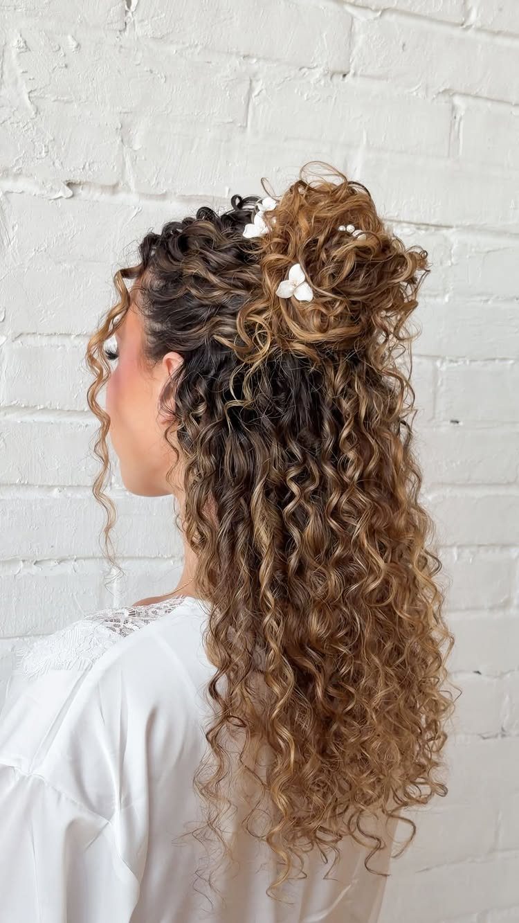 Woman with curly brown hair in a half-up bun with white flowers