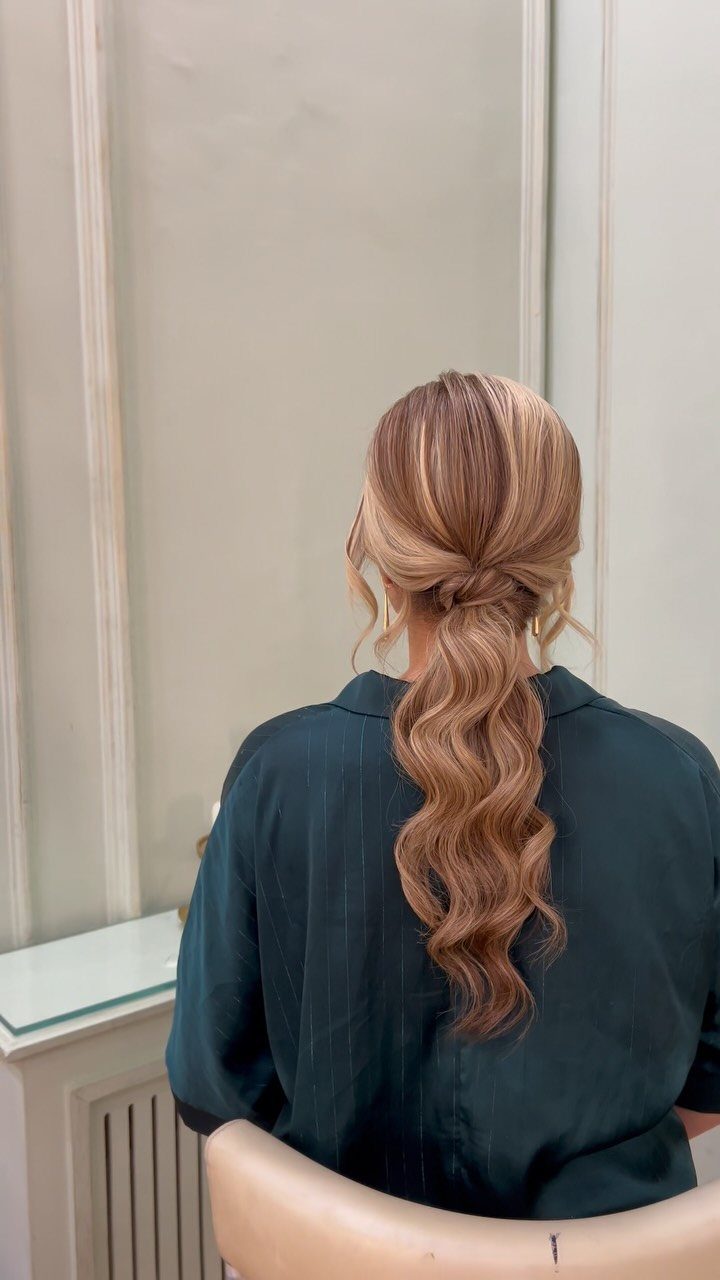 Blonde medium hair styled in a low ponytail with romantic wavy curls.