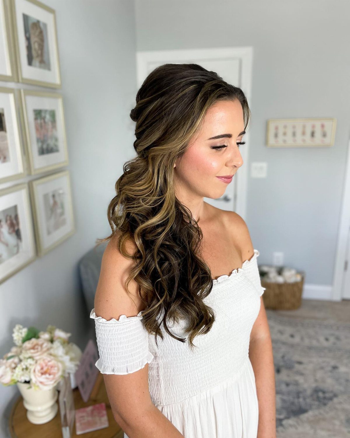 Woman with brown hair styled in side-swept curls wearing a white off-the-shoulder dress.