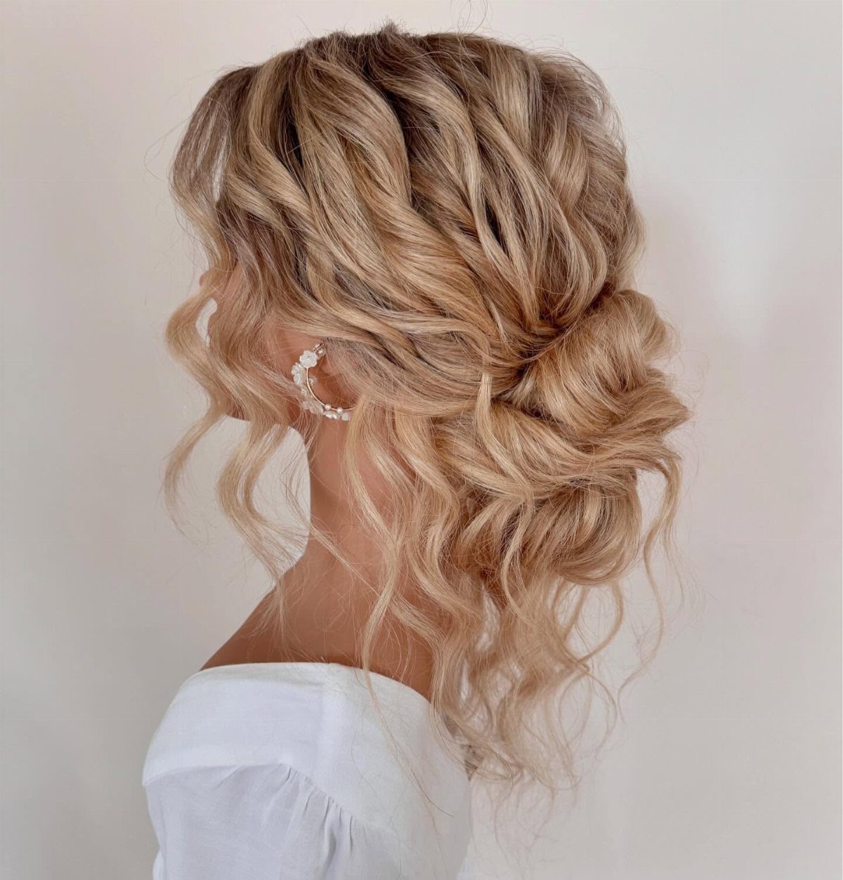 Blonde woman with a textured low bun and loose curly face-framing strands.