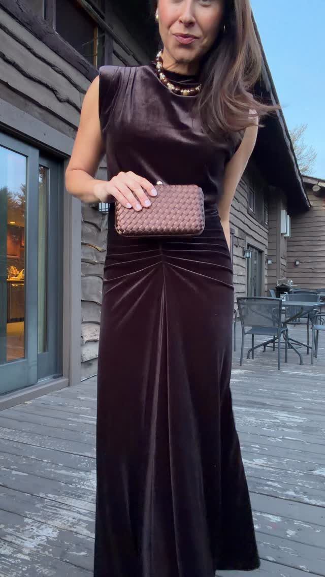 Wedding Outfit Outdoor: 9 Guest Looks for Every Setting 8 Woman in a long dark brown velvet dress holding a woven clutch on a wooden deck.