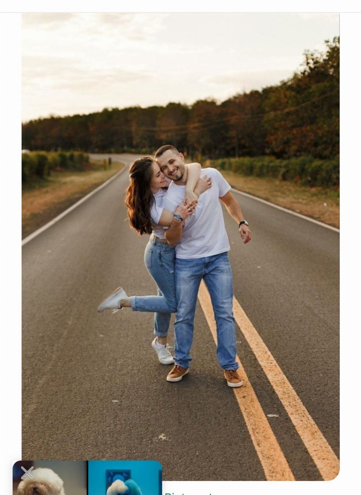 A happy couple in casual white shirts and blue jeans posing on a road at sunset.