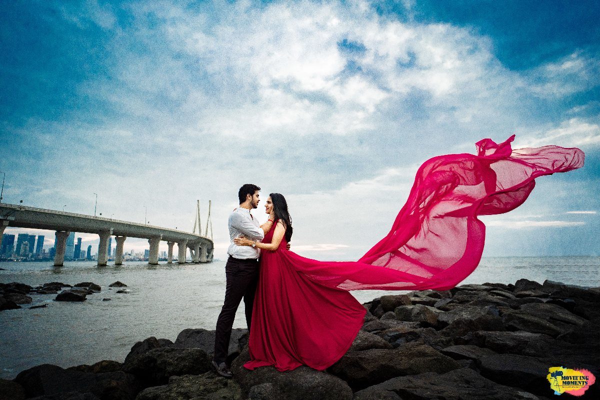 A couple posing on a rocky coast with a woman wearing a long flowing red dress.