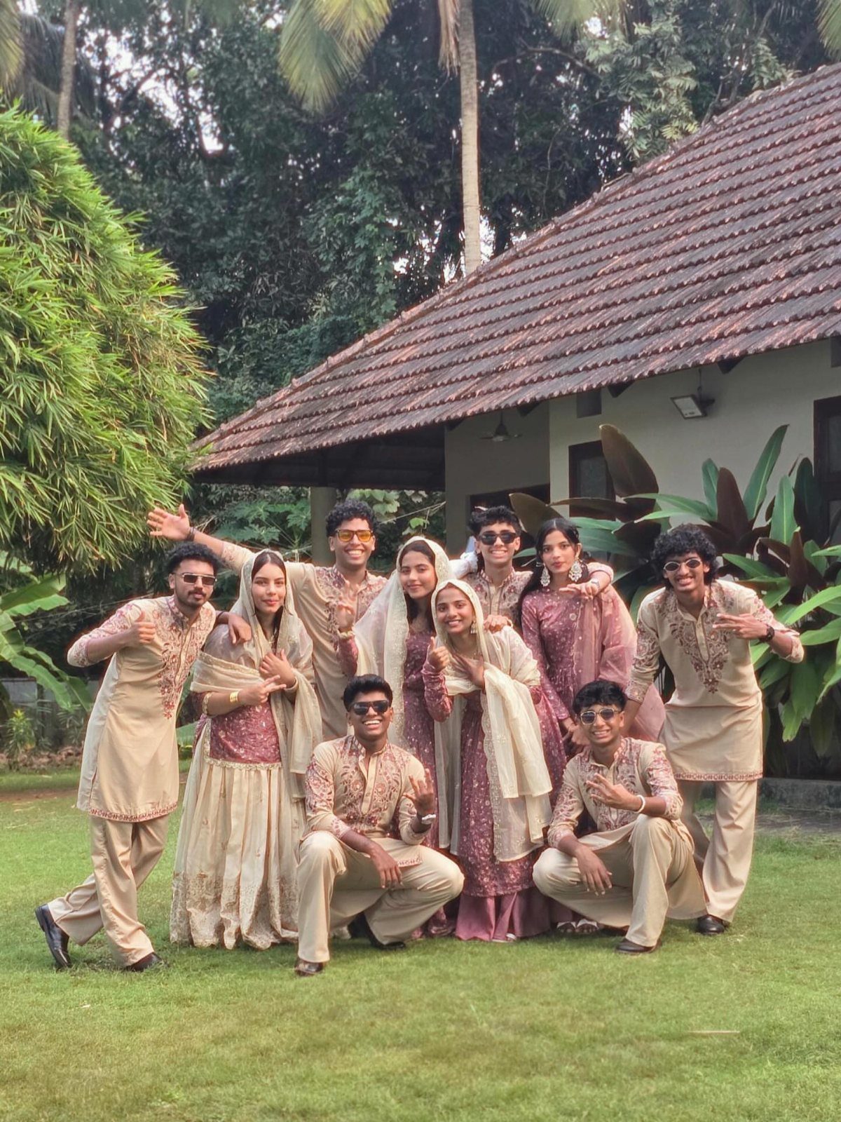 18 Wedding Outfit Theme Ideas for 2026: Beach, Boho, Gatsby & More 19 Group of people in cream and maroon traditional South Asian attire posing on a lawn.
