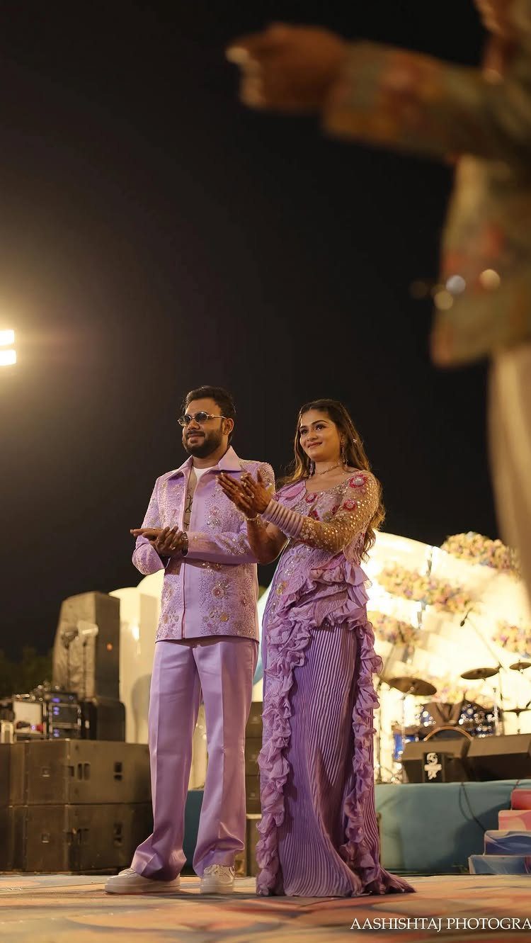 18 Wedding Outfit Theme Ideas for 2026: Beach, Boho, Gatsby & More 15 A man and woman dressed in matching lavender outfits posing on an outdoor stage at night.