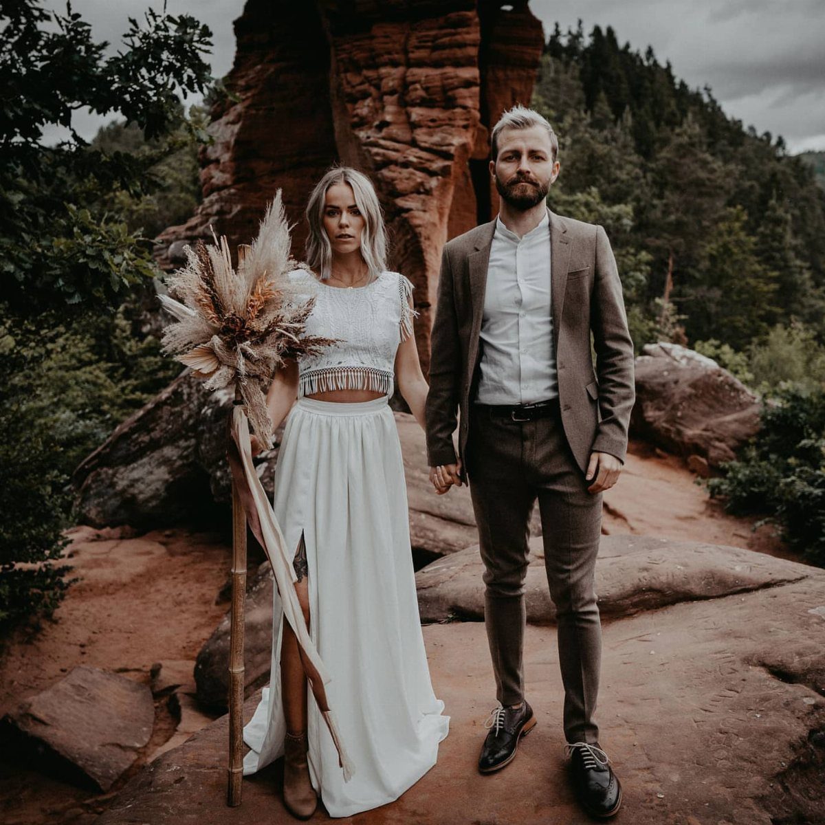 18 Wedding Outfit Theme Ideas for 2026: Beach, Boho, Gatsby & More 6 A couple posing in rustic wedding attire against a backdrop of red rocks and forest.