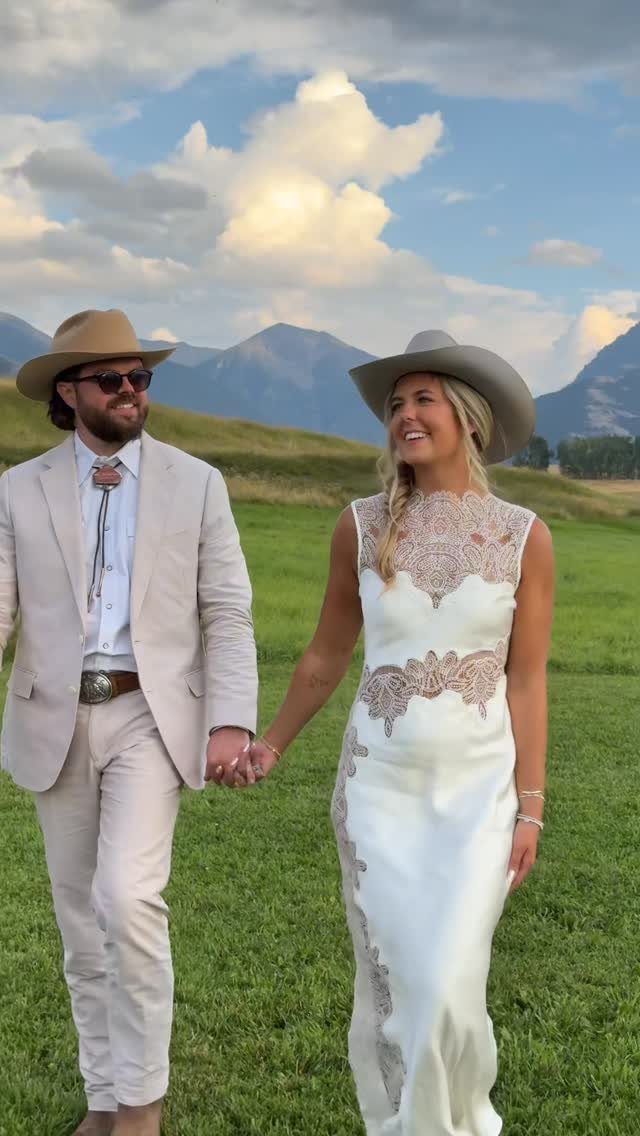 18 Wedding Outfit Theme Ideas for 2026: Beach, Boho, Gatsby & More 14 A man in a tan suit and a woman in a white embroidered dress walking through a field.