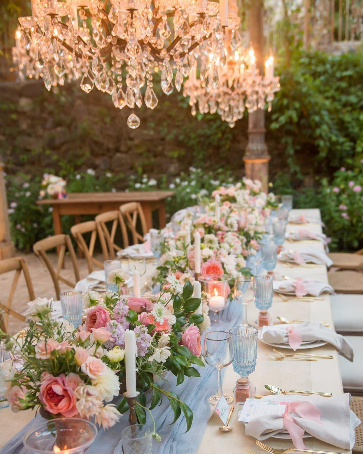 Wedding Party Colors: 13 Real Palette Ideas for Your Bridal Party 4 A long wedding table decorated with pink flowers, blue runners, and crystal chandeliers outdoors.