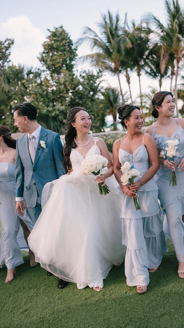 Wedding Party Colors: 13 Real Palette Ideas for Your Bridal Party 7 A bride and groom walking with bridesmaids in light blue dresses on a tropical lawn.