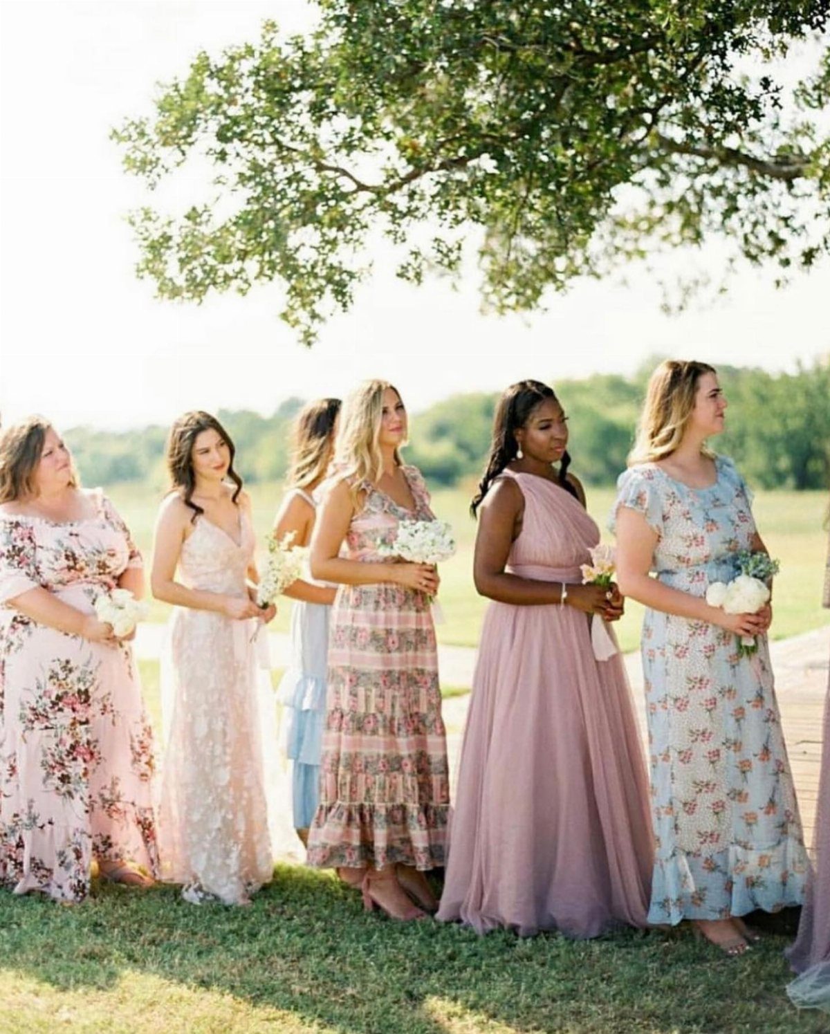 Wedding Party Colors: 13 Real Palette Ideas for Your Bridal Party 12 Six bridesmaids in various floral and pastel colored dresses standing in a line outdoors holding bouquets.
