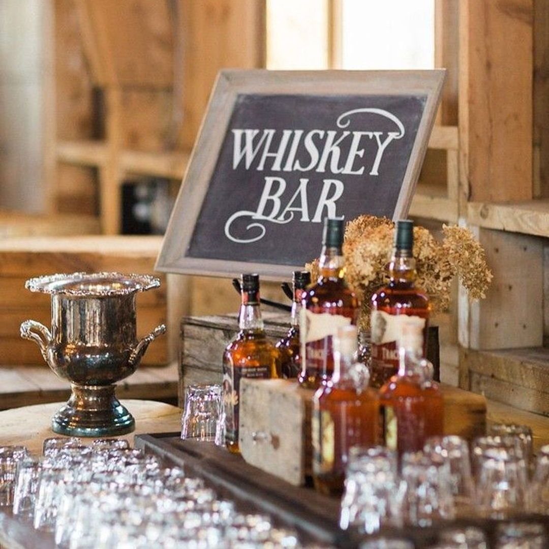 10 Wedding Party Ideas for an Unforgettable Night 4 Whiskey bottles and glasses arranged on a table next to a whiskey bar chalkboard sign.