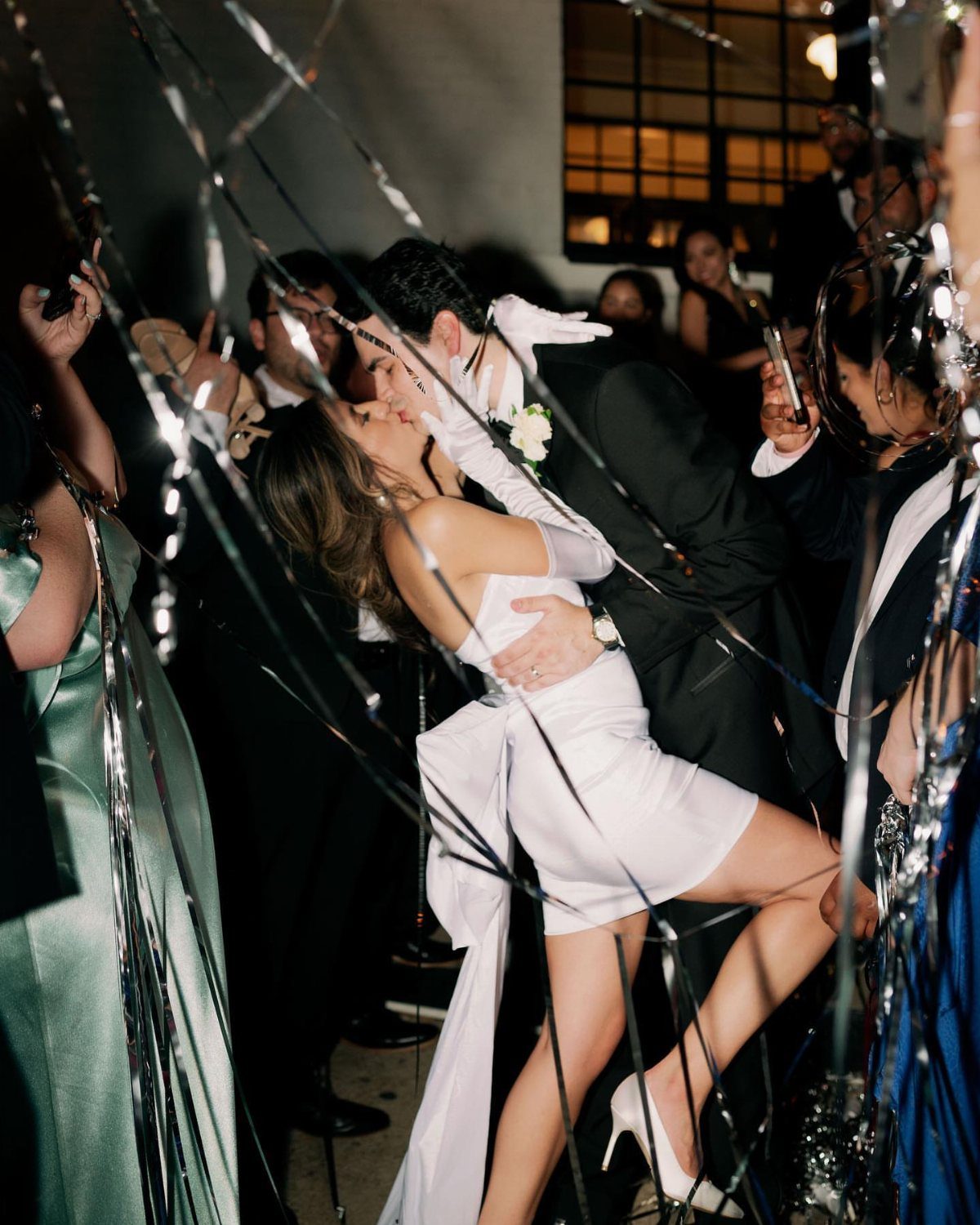 Groom in tuxedo dipping and kissing bride in short white wedding dress.
