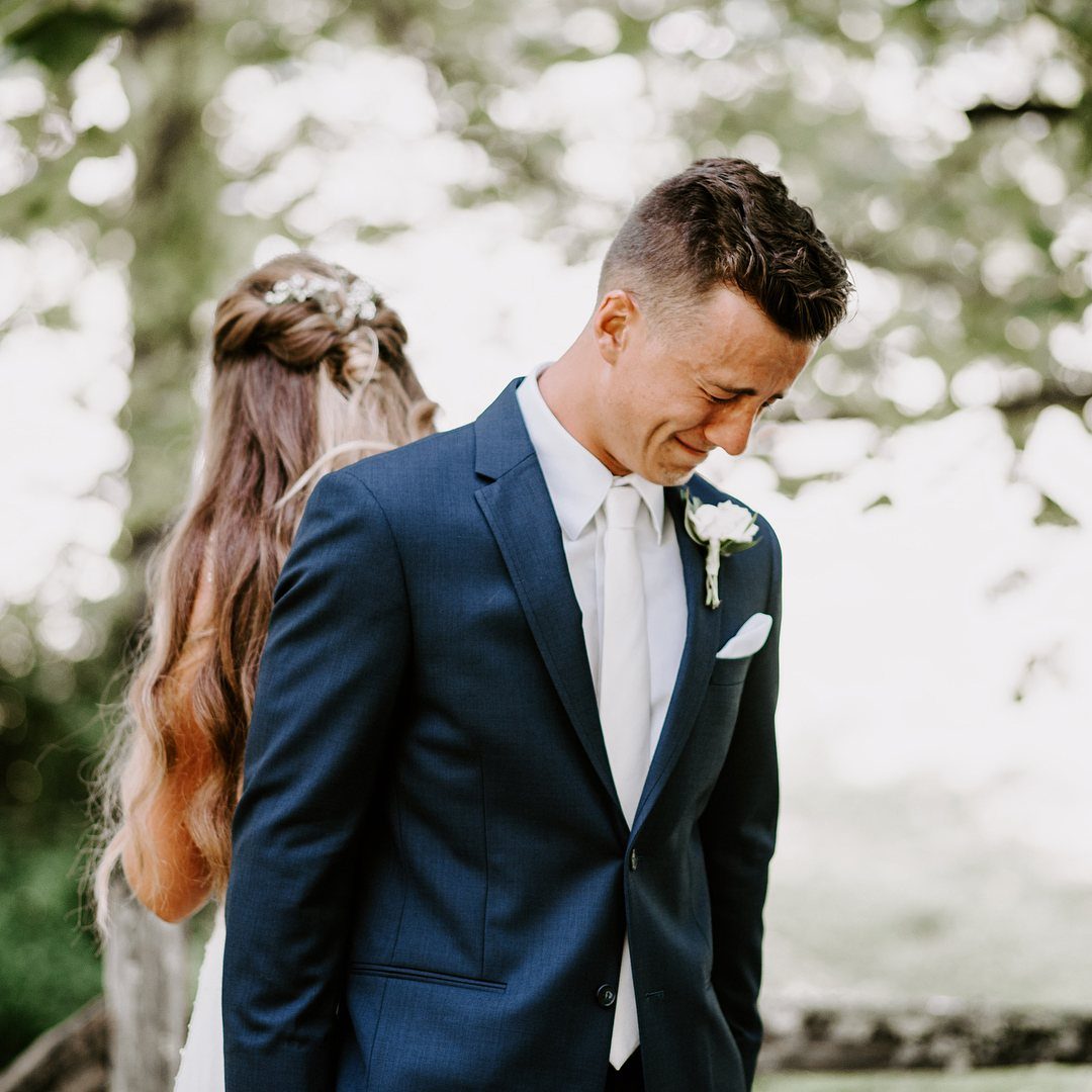 Emotional groom in navy suit reacting to his bride in an outdoor setting