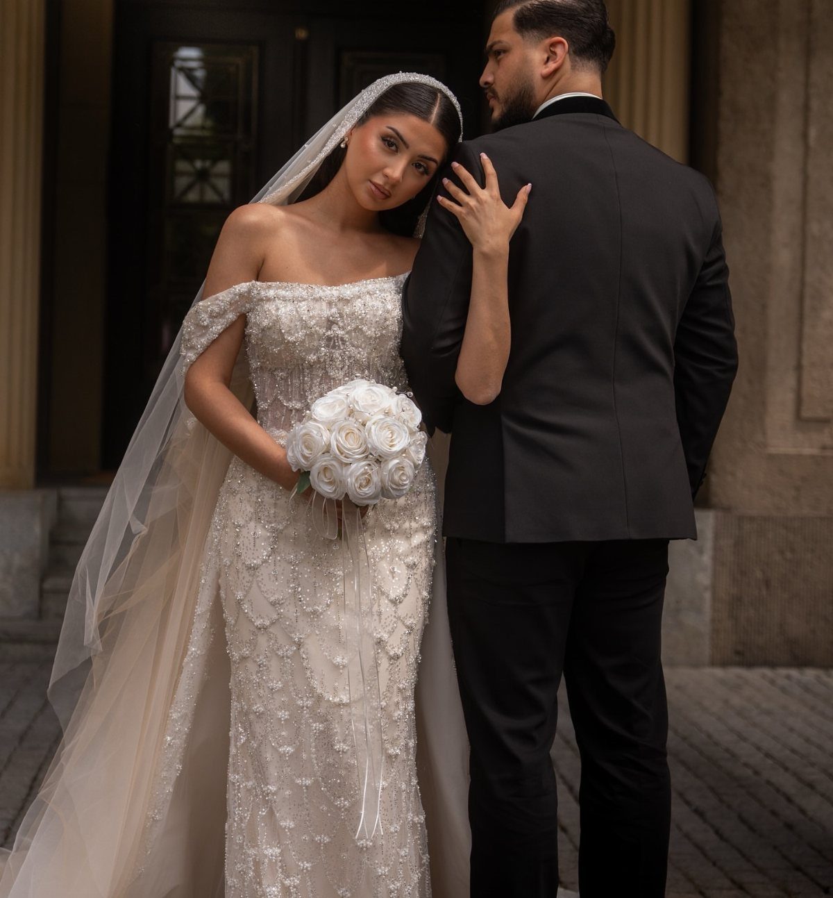 Bride in beaded gown leaning her head on the groom's shoulder outdoors