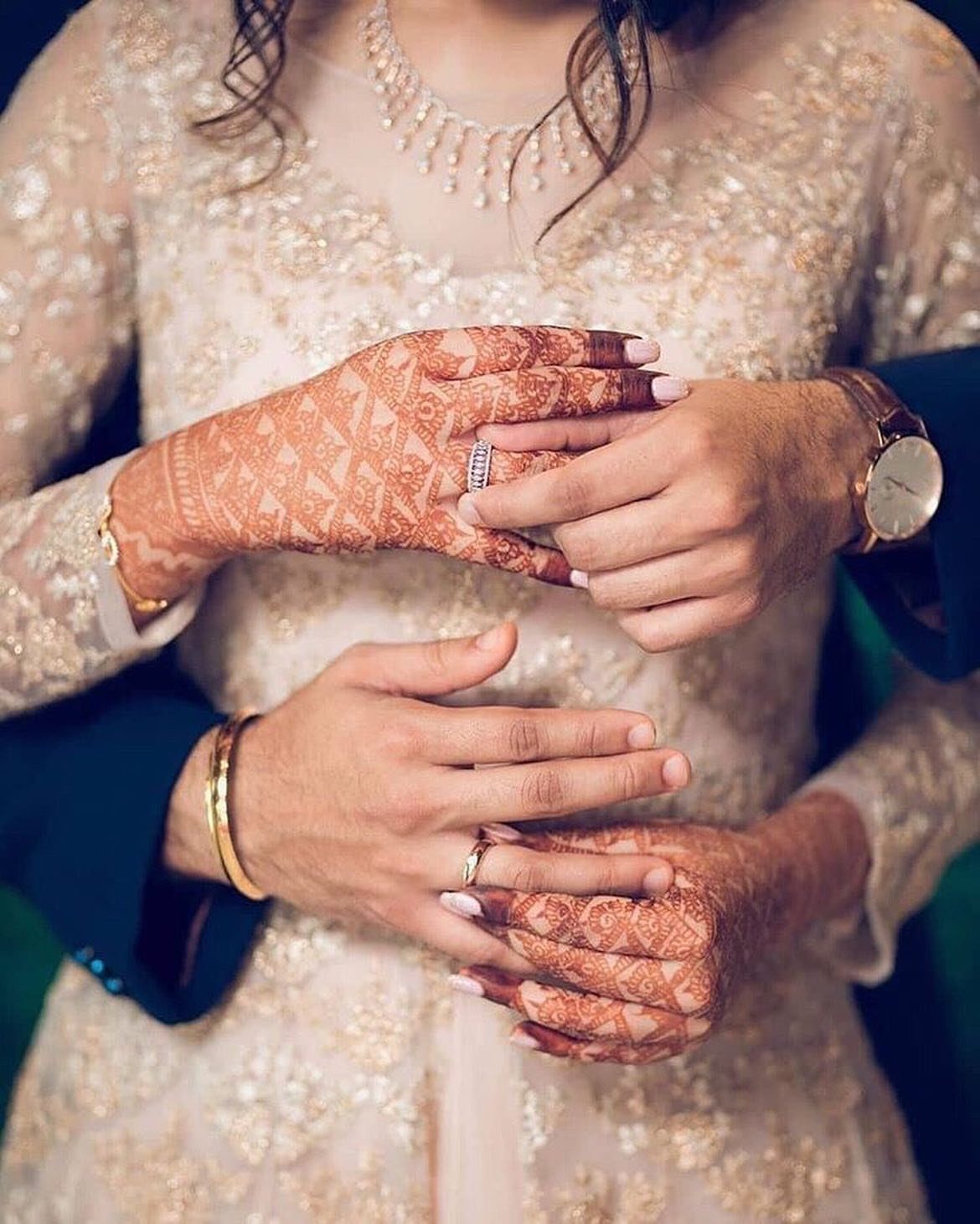 Couple's hands with wedding rings and henna resting on an embroidered bridal gown