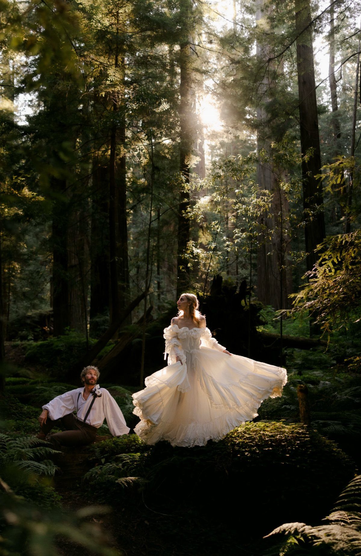 Bride in white gown and groom in forest framed by tall redwood trees