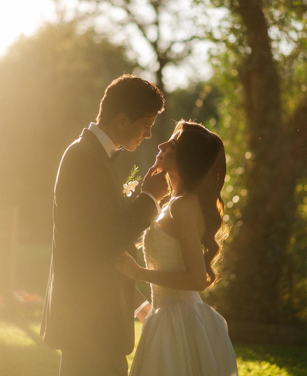Bride and groom facing each other closely in a sunlit garden setting.