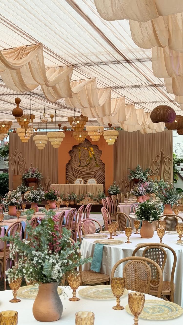 Wedding reception tables with beige drapes, wicker chairs, and terracotta floral centerpieces.