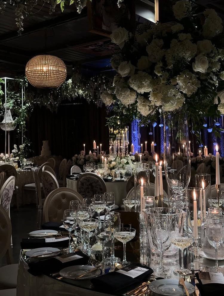 Formal wedding table with black napkins, champagne linens, white flowers, and glowing candles.