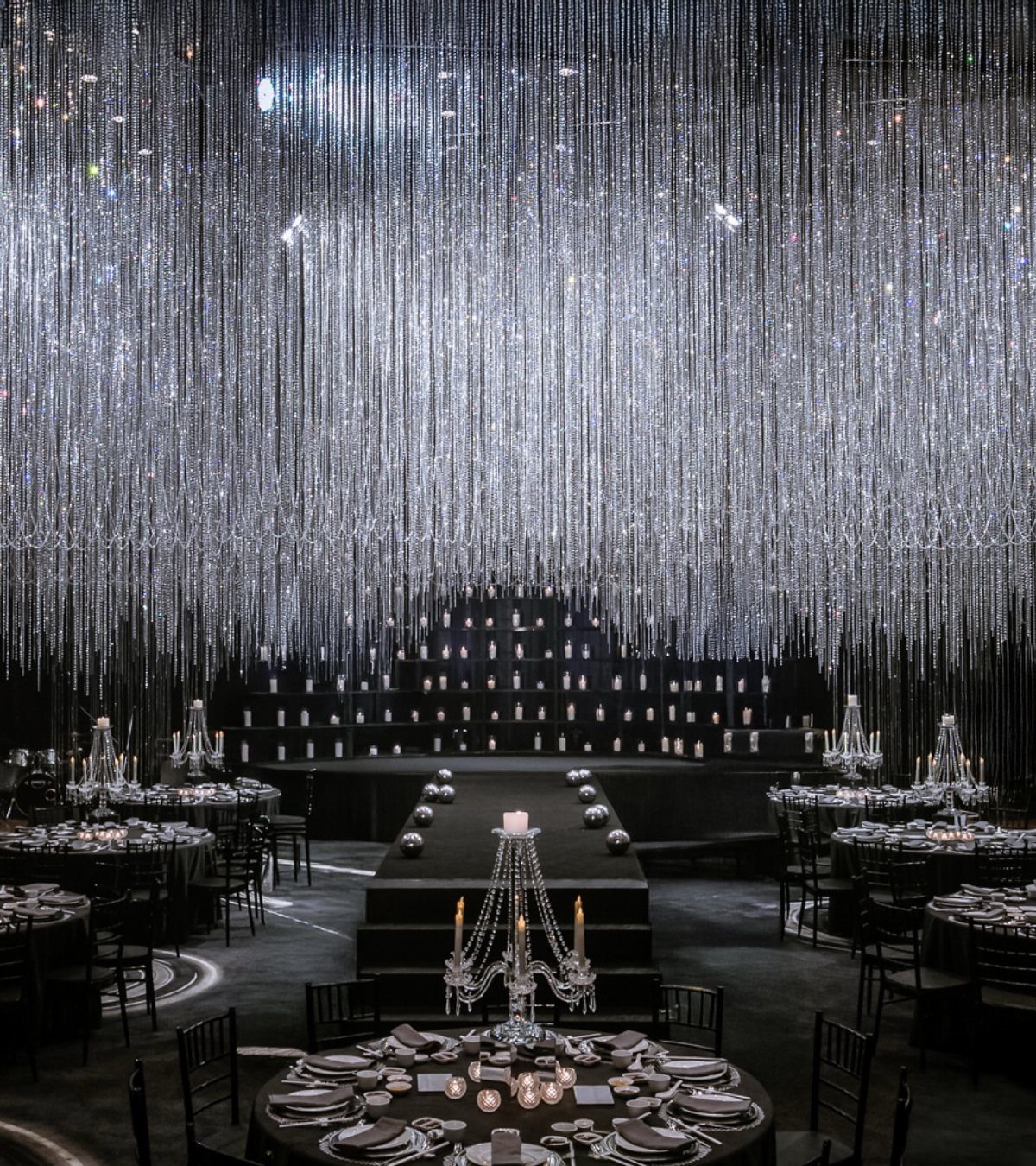 Black wedding reception tables with crystal candelabras under a shimmering silver beaded ceiling.