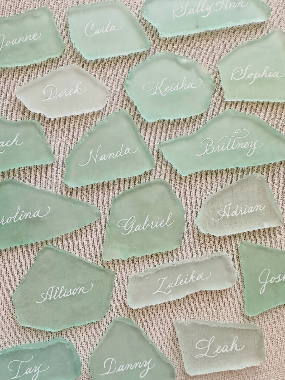 Sea glass place cards with white cursive names on a beige fabric background