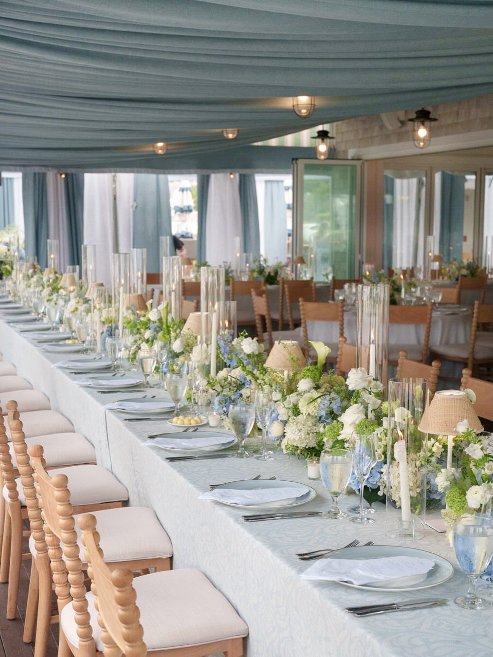 Long wedding table with light blue linens and white and blue floral centerpieces.