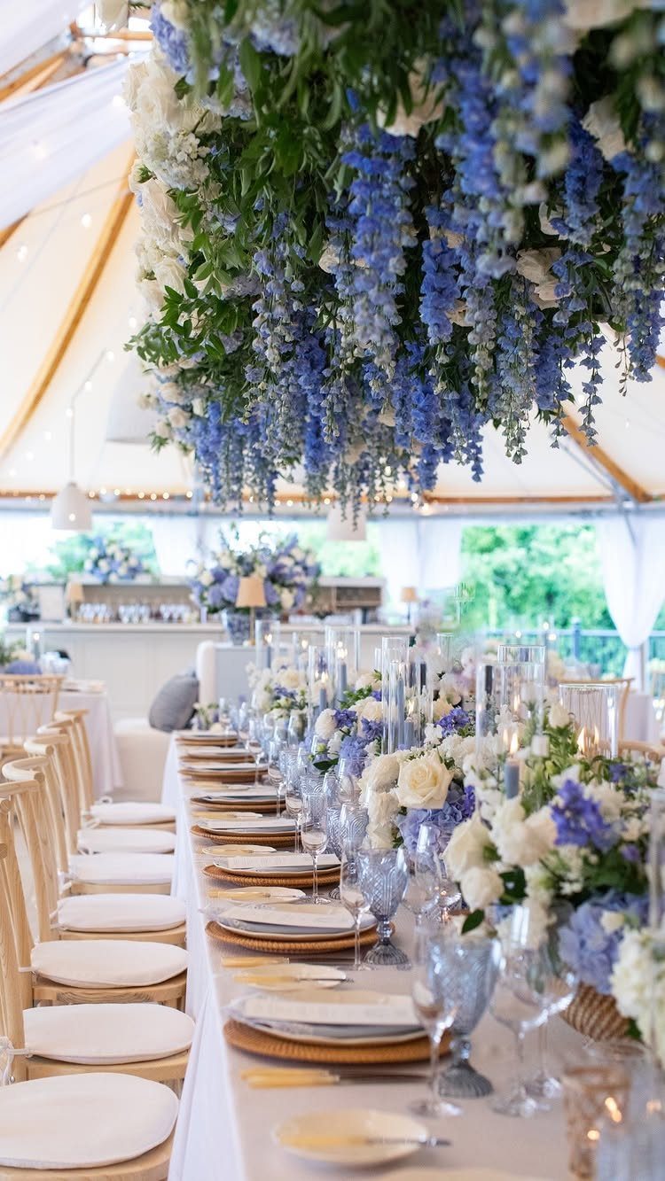 Wedding reception table with white linens and blue and white floral centerpieces and overhead installations.