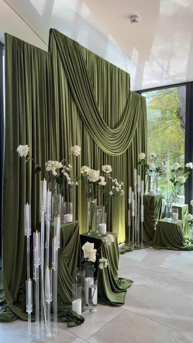 Olive green draped fabric backdrop with white roses and tall glass candle holders.