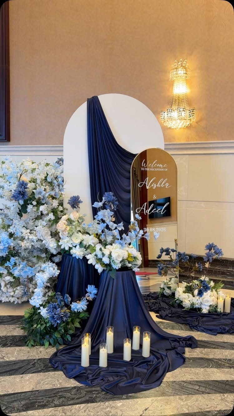 Navy blue and white wedding reception decor with flowers, candles, and a welcome mirror.