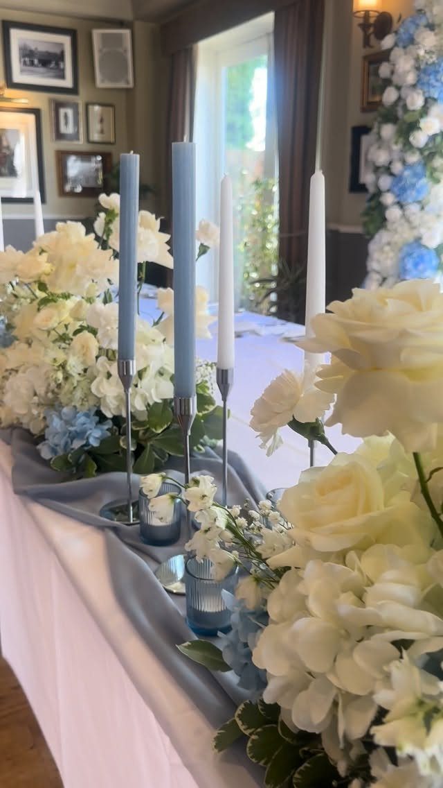 Wedding table with pale blue candles, silver holders, and white floral arrangements.
