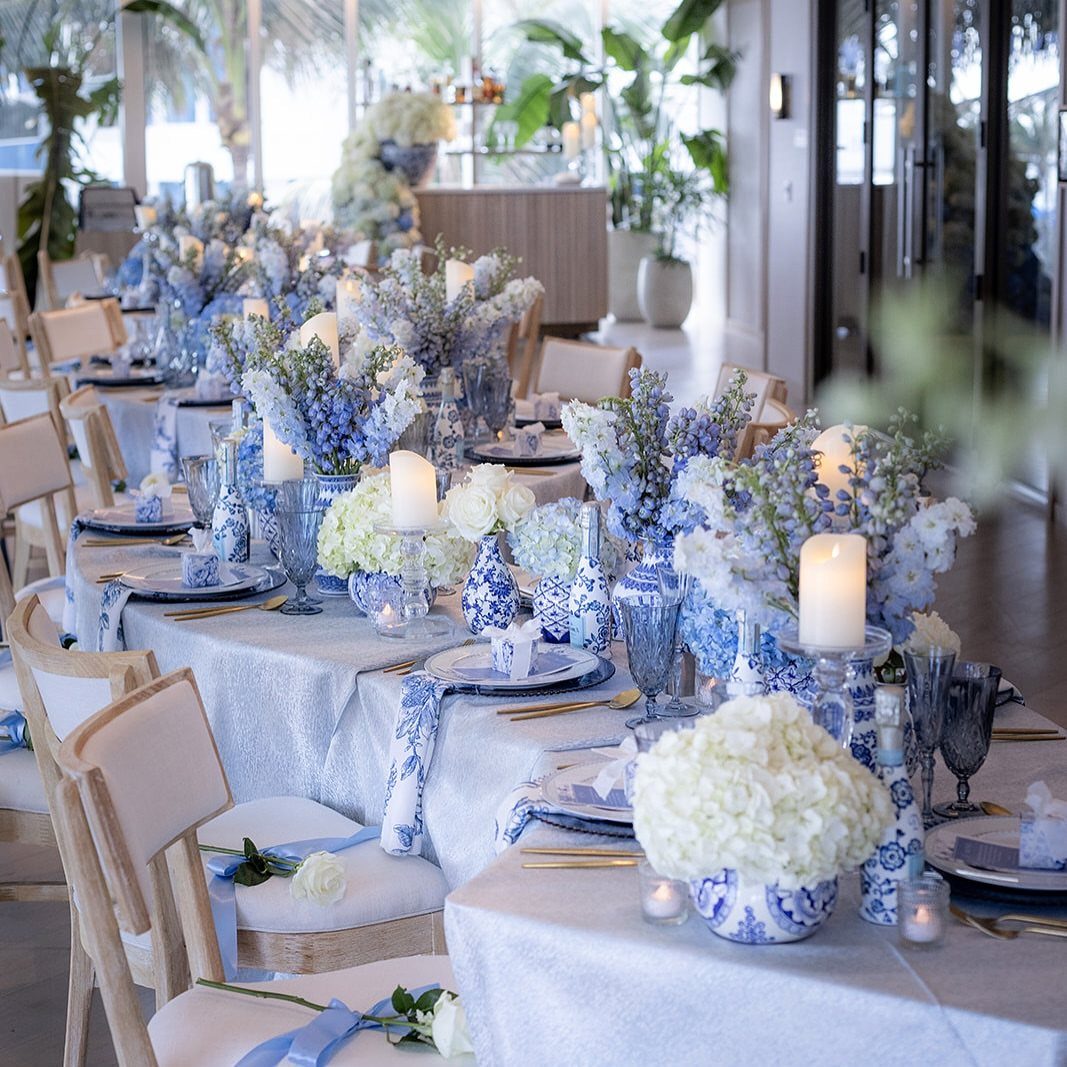 Wedding reception table with periwinkle blue and ivory linens, blue floral centerpieces and candles.