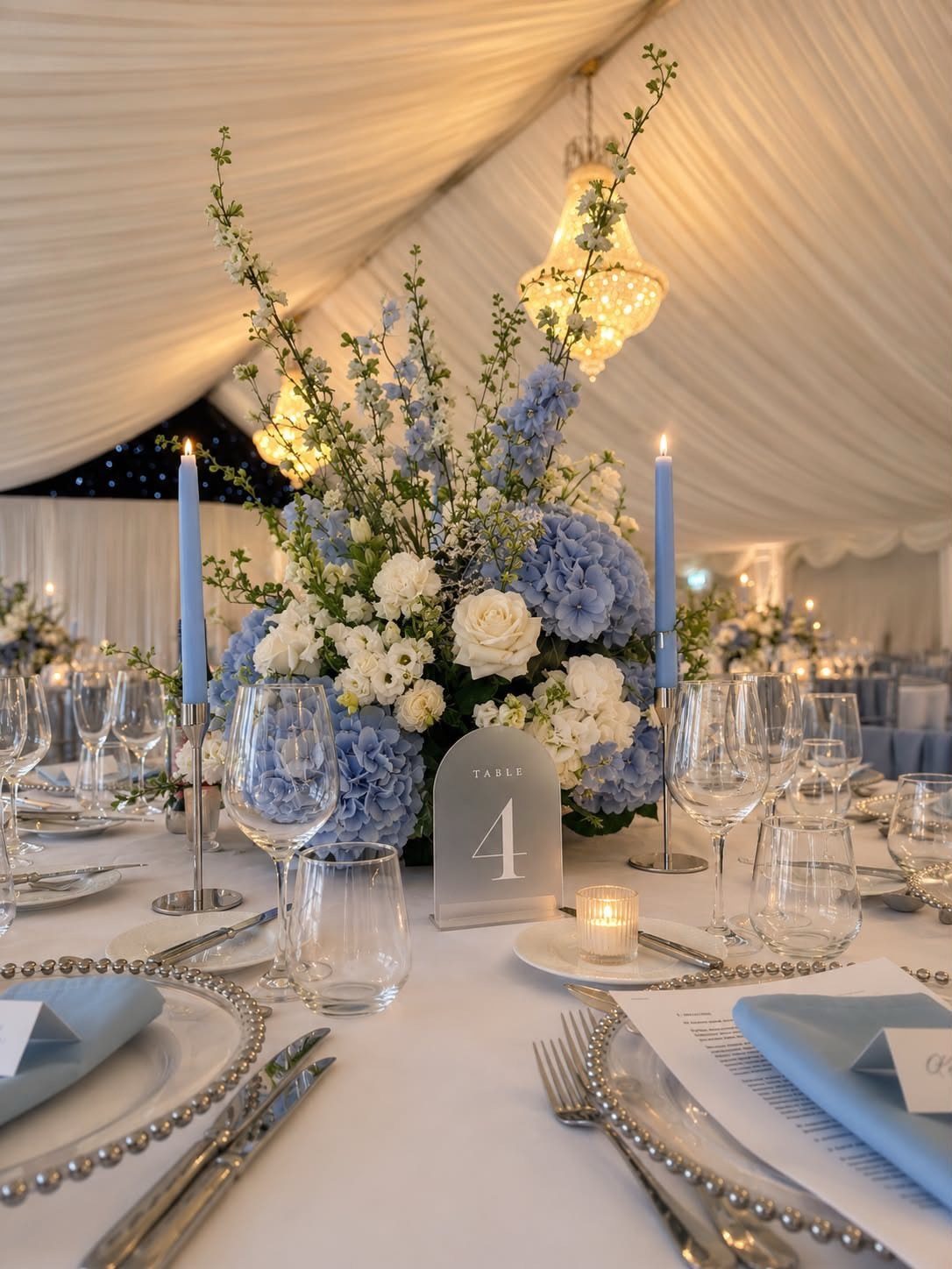 Wedding table setting with powder blue napkins, blue hydrangeas, and tall blue candles.