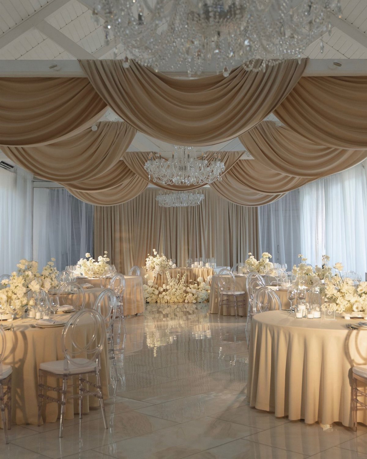 Champagne draped ceiling and tables with white flowers in a luxury wedding reception hall