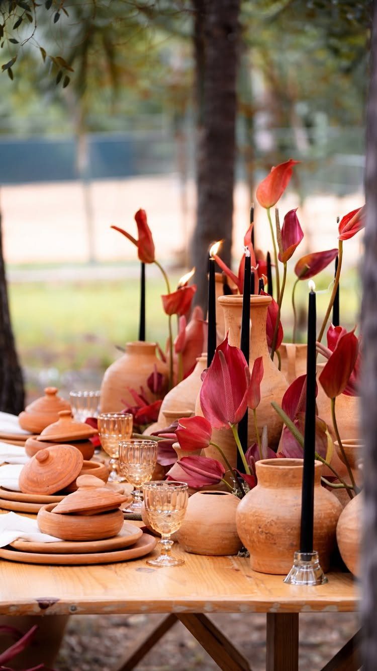 Terracotta pottery and red flowers with black candles on a wooden wedding table.