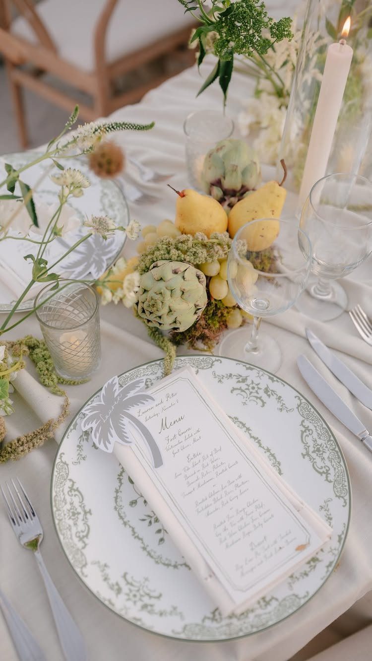 Wedding table setting with white plates, green floral accents, and yellow pear centerpiece.