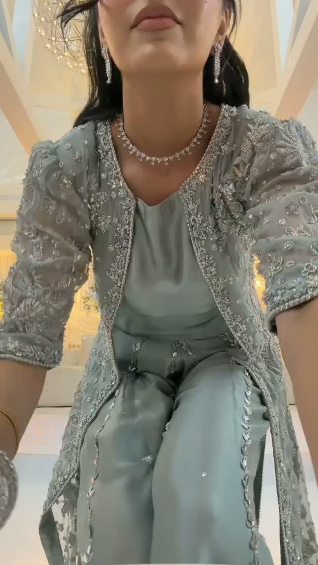 Woman wearing an embellished sage green formal outfit with a beaded lace jacket and sparkling jewelry.